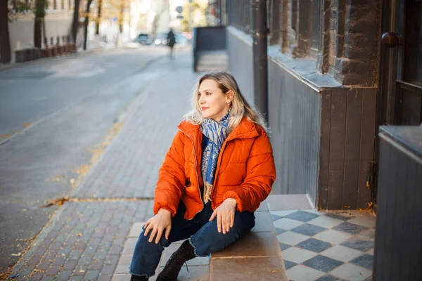 Glücklich Lächelnde Frau Mittleren Alters Orangefarbener Daunenjacke Sitzt Draußen Auf — Stockfoto