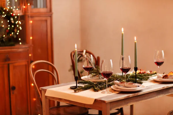 在家里的圣诞庆祝活动中 放在盘子和针叶树下的点燃的蜡烛和红酒杯 — 图库照片