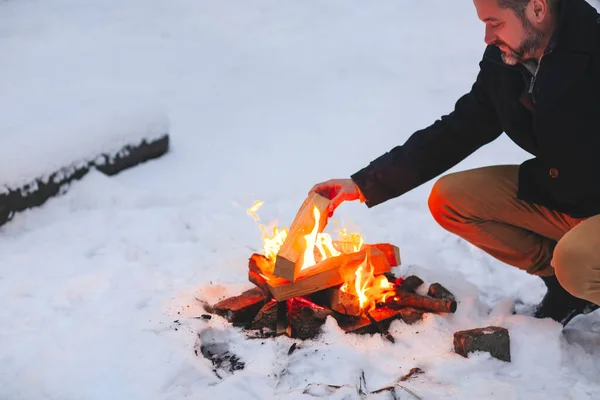 寒い冬の夜に雪の森の中でキャンプファイヤーをした後に火で手を暖めて成熟した男は 悪天候の中で良いと快適に感じるために熱を使用して 冬の休日を楽しんで — ストック写真