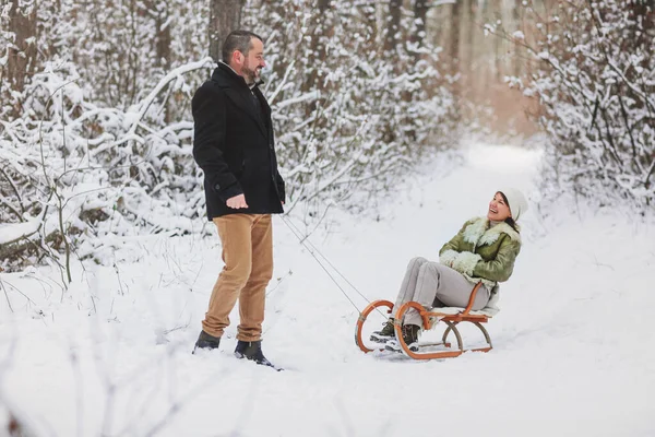 快乐嬉闹的成熟家庭夫妇在冬季公园滑行 一起玩乐 积极的中年妇女坐在雪橇上 而她的丈夫从后面推着她 户外活动 — 图库照片