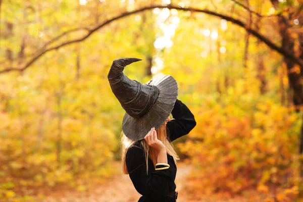万圣节当天 穿着巫婆服装的金发女人在森林里走着 路上布满了秋天的树叶 — 图库照片