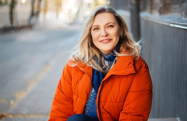 Glücklich Lächelnde Frau Mittleren Alters Orangefarbener Daunenjacke Sitzt Draußen Auf — Stockfoto