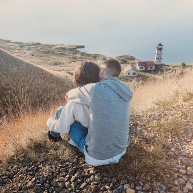 Gün batımında deniz fenerinin yanında samimi kazaklar giymiş romantik bir çift. 