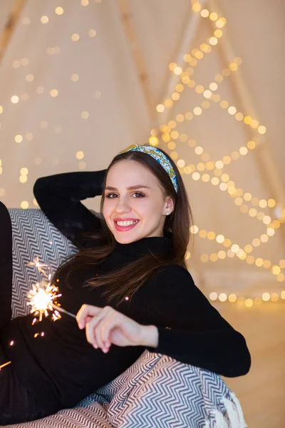 欢快的年轻女性 闪烁着闪光的火花 一杯香槟紧靠着闪闪发光的圣诞树站在柔软的焦点上 — 图库照片