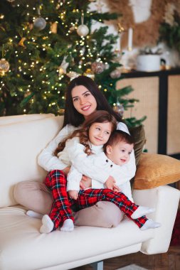 Evde Noel kutlaması sırasında kozalaklı ağacın yanında çocuklu bir kadın. Tatil ve aile kavramı