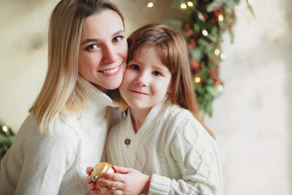 居心地の良いニットのセーターで楽しい母親と素敵な女の子の娘は リビングルームで新年の泡やおもちゃでクリスマスモミの木を飾る 冬の休日の笑顔の雰囲気を感じます 家族の休日 — ストック写真