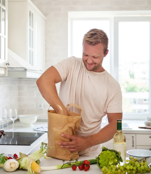 Homem segurando saco de papel cheio de mantimentos na cozinha — Fotografia de Stock