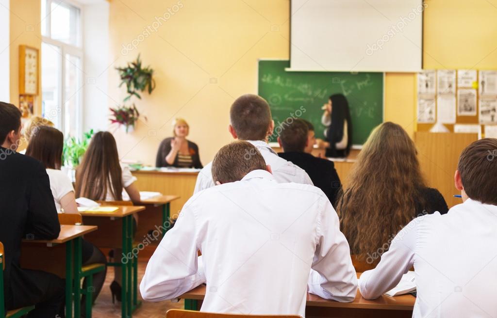 Rear view of students listening to female student near the desk 