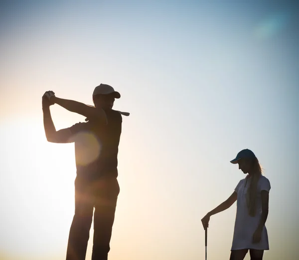 Erkek ve kadın golfçüler sunset at — Stok fotoğraf