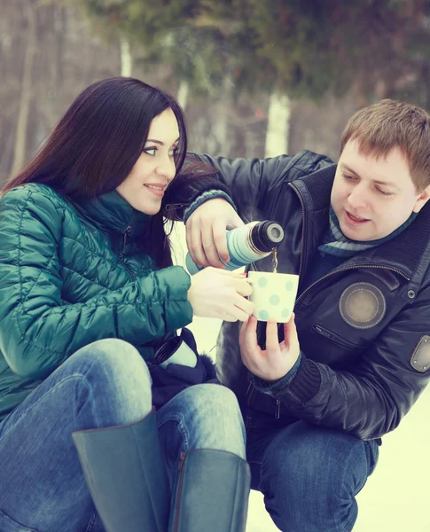 Счастливая пара веселится в зимнем парке, пьет горячий чай. — стоковое фото