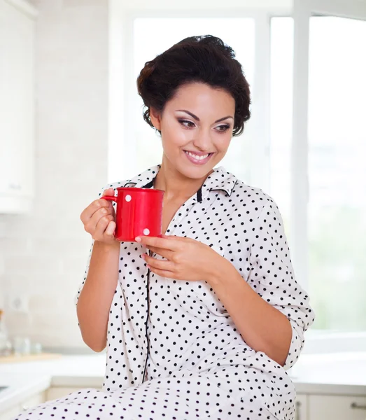 Šťastná žena drží šálek kávy ve své kuchyni — Stock fotografie