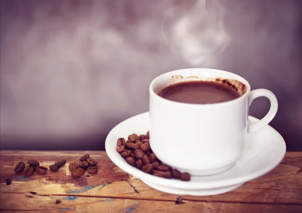 Kávový pohár a kávová zrna na dřevěném stole — Stock fotografie
