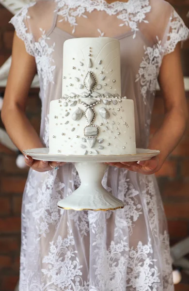 Sposa in piedi vicino al muro di mattoni che tiene torta nuziale — Foto Stock