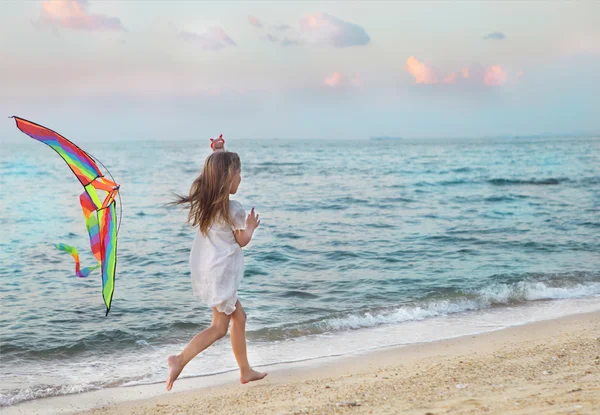 Маленькая девочка с летающим воздушным змеем на пляже на закате — стоковое фото