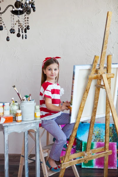 Kleines Künstlermädchen mit Pinsel und Blick über eine Leinwand — Stockfoto
