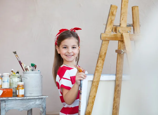 Bir boya fırçası tutan ve bir canva üzerinde seyir küçük sanatçı kız — Stok fotoğraf