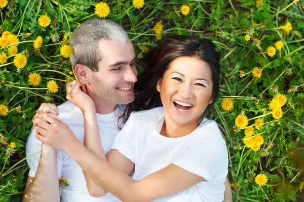 Young loving couple lying at the green grass with dandelion — Stock Photo, Image