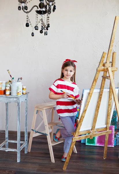 Kleines Künstlermädchen mit Pinsel und Blick über eine Leinwand — Stockfoto