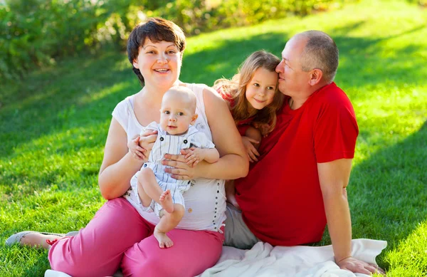 Familia feliz con dos niños sentados en la hierba — Foto de Stock