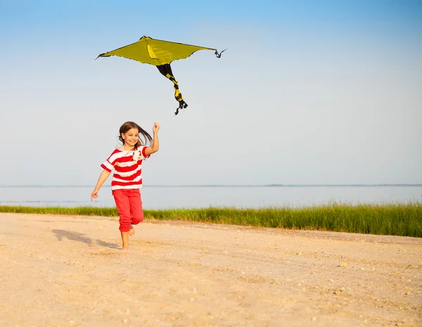 Little running girl with flying kite on beach at sunset — Stock Photo, Image