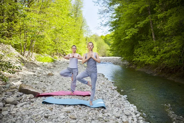 Iki kadın dağ nehir tarafından yoga uygulamak — Stok fotoğraf