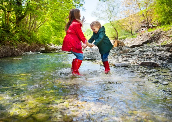 Dzieci do noszenia kalosze skoki do rzeki górskie — Zdjęcie stockowe