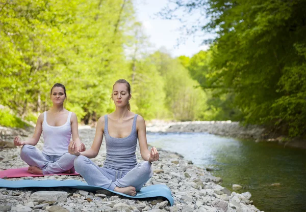 Dos mujeres practican yoga junto al río de la montaña —  Fotos de Stock