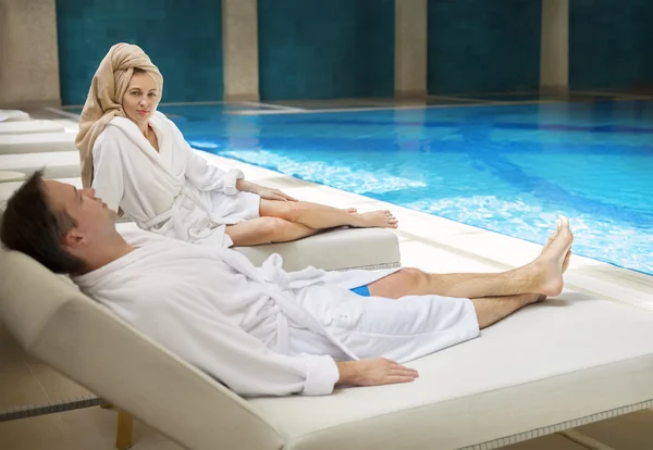 Casal relaxante à beira da piscina vestindo roupões de banho — Fotografia de Stock