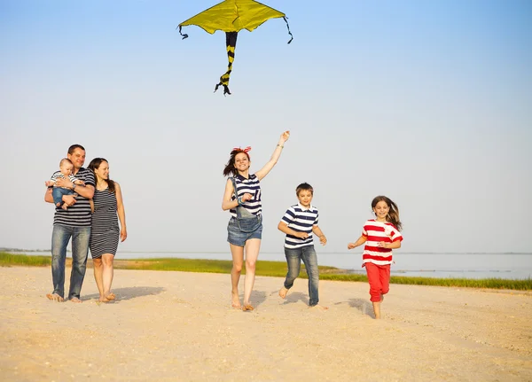 Glückliche junge Familie mit einem Drachen am Strand — Stockfoto
