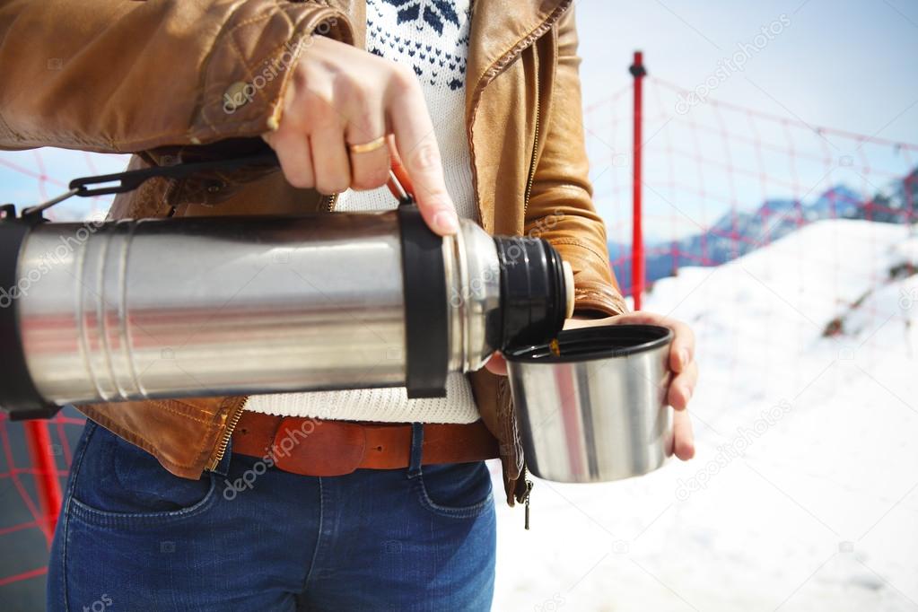 Young woman holding thermos on mountain top in winter