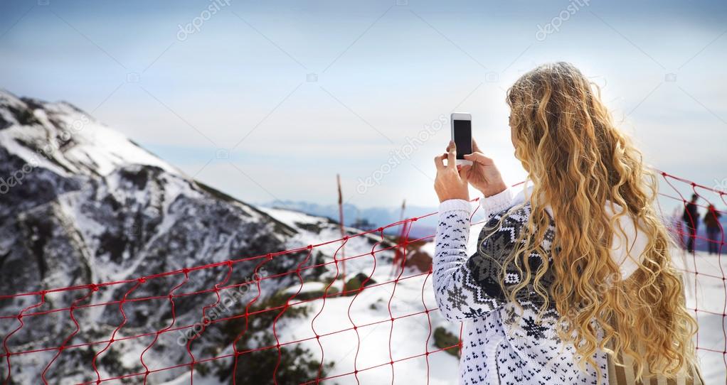 Woman photographing winter landscape mountains and snow with cel