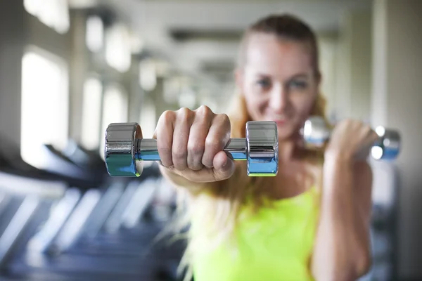 Jonge vrouw met halters op gym achtergrond — Stockfoto