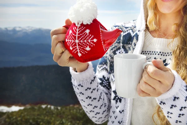 Tea pot in the knotted cap and cup in the hands of a woman — Stock Photo, Image