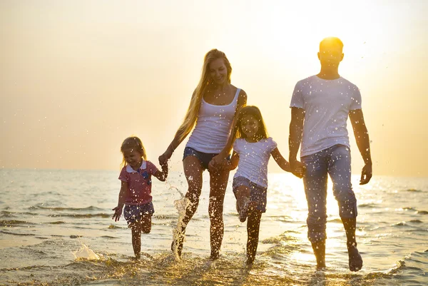 Feliz jovem família se divertindo correndo na praia ao pôr do sol. Família — Fotografia de Stock