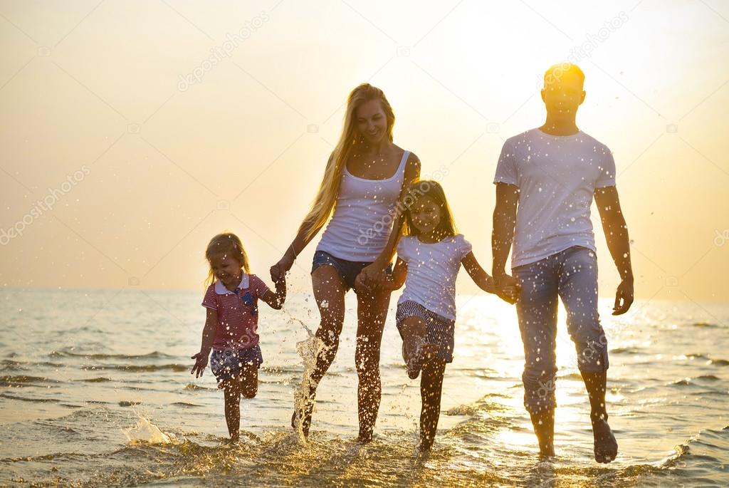 Happy young family having fun running on beach at sunset. Family