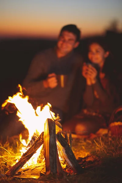 Portrait of the happy couple sitting by fire on autumn beach at — Stock Photo, Image