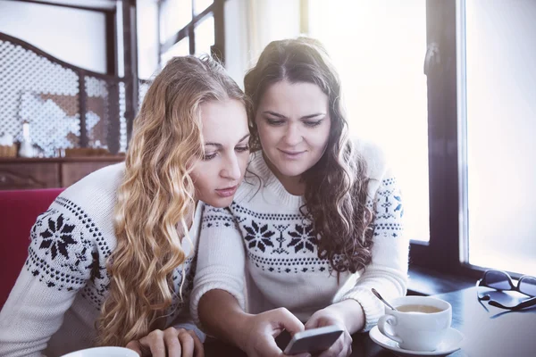 Glada kvinnor tittar till rörlig telefonerna i ett café — Stockfoto