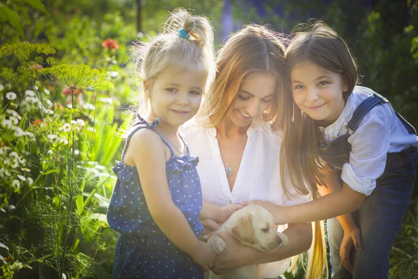 Happy woman and her daughters with puppy of labrador — Stock Photo, Image