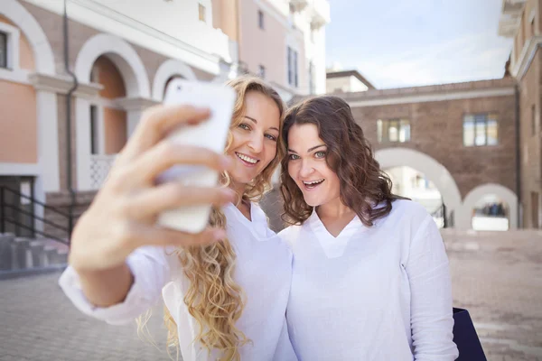 Duas jovens mulheres com sacos de compras tirando uma selfie — Fotografia de Stock