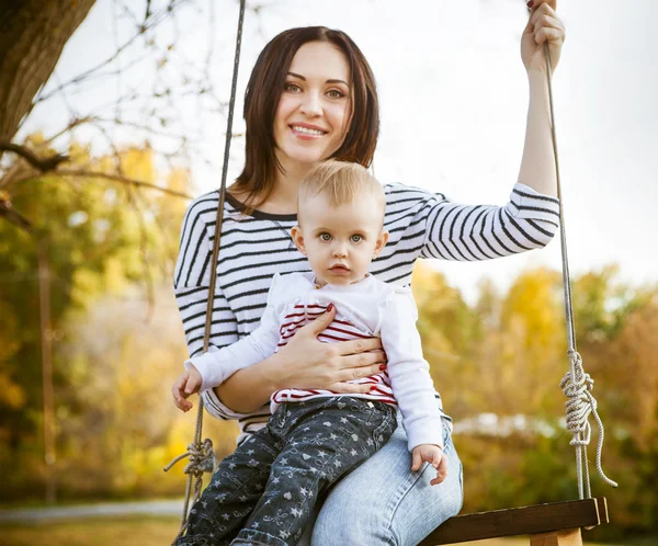 Mãe feliz e seu pequeno balanço do bebê no parque de outono — Fotografia de Stock