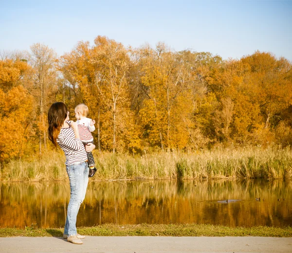 Moeder en baby op herfst meer glimlachen — Stockfoto