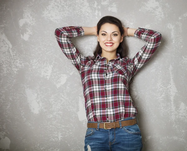 Happy woman leaning against a gray wall looking at camera — Stock Photo, Image