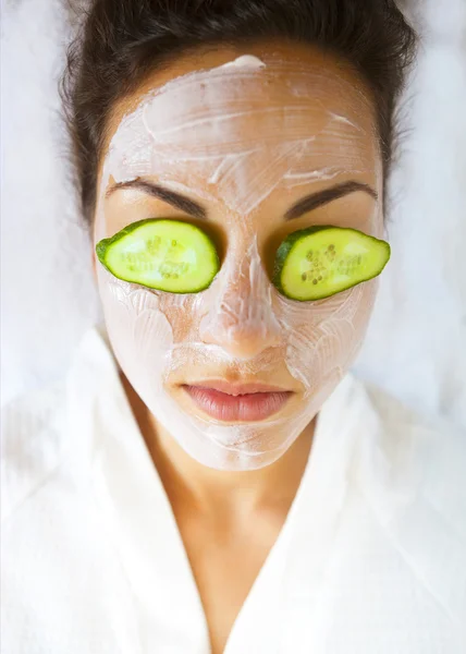 Giovane donna con una maschera facciale e cetriolo sul viso — Foto Stock