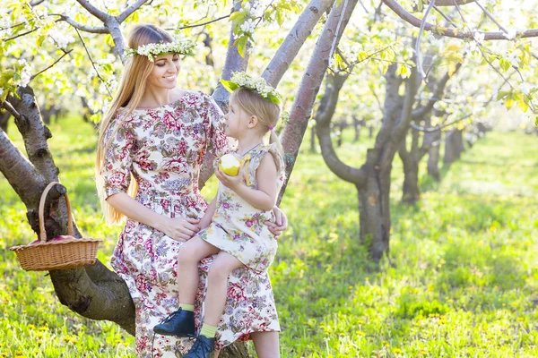 Glad mamma och hennes lilla dotter i en blommande trädgård — Stockfoto