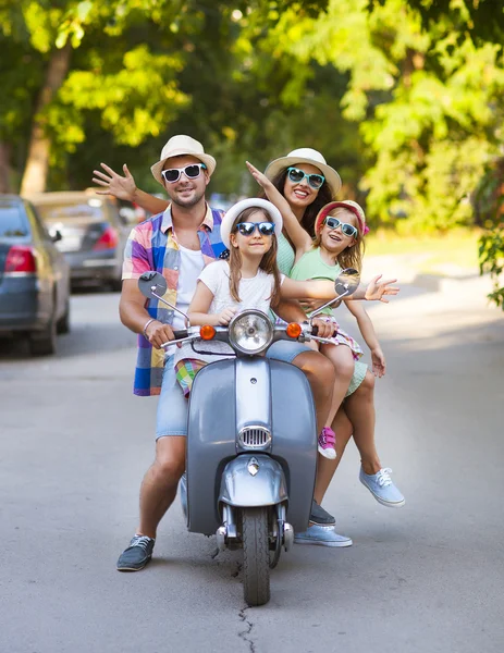 Gelukkige jonge familie rijden een vintage scooter in de straat wearin — Stockfoto