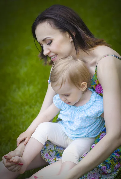 Vacker ung mamma med dotter avkopplande sitter på gräset — Stockfoto