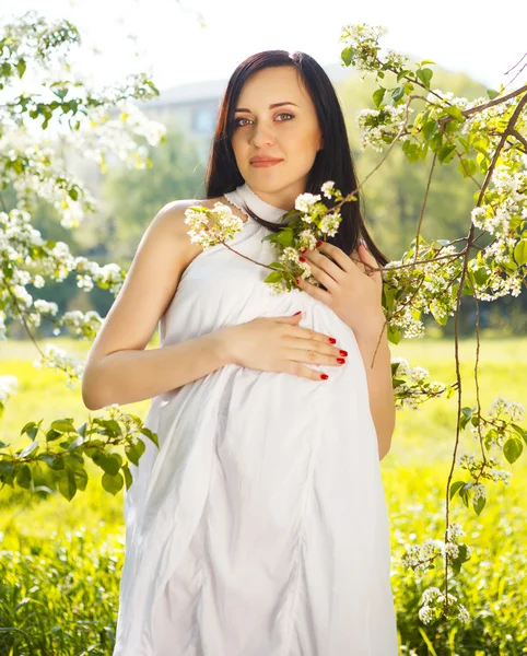 Bella donna incinta in abito bianco nella primavera fiorita — Foto Stock