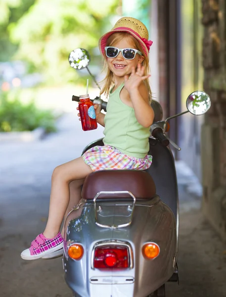 Feliz niña sentada en un scooter vintage en la calle nos —  Fotos de Stock