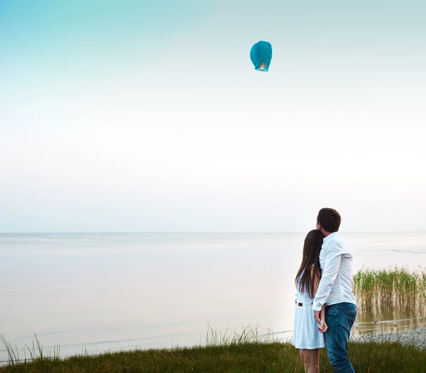 Pareja joven comienza una linterna verde del cielo chino en el atardecer — Foto de Stock