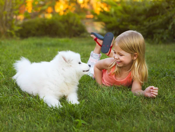 Little smiling girl playing with Samoyed puppy in the summer gar — Stock Photo, Image